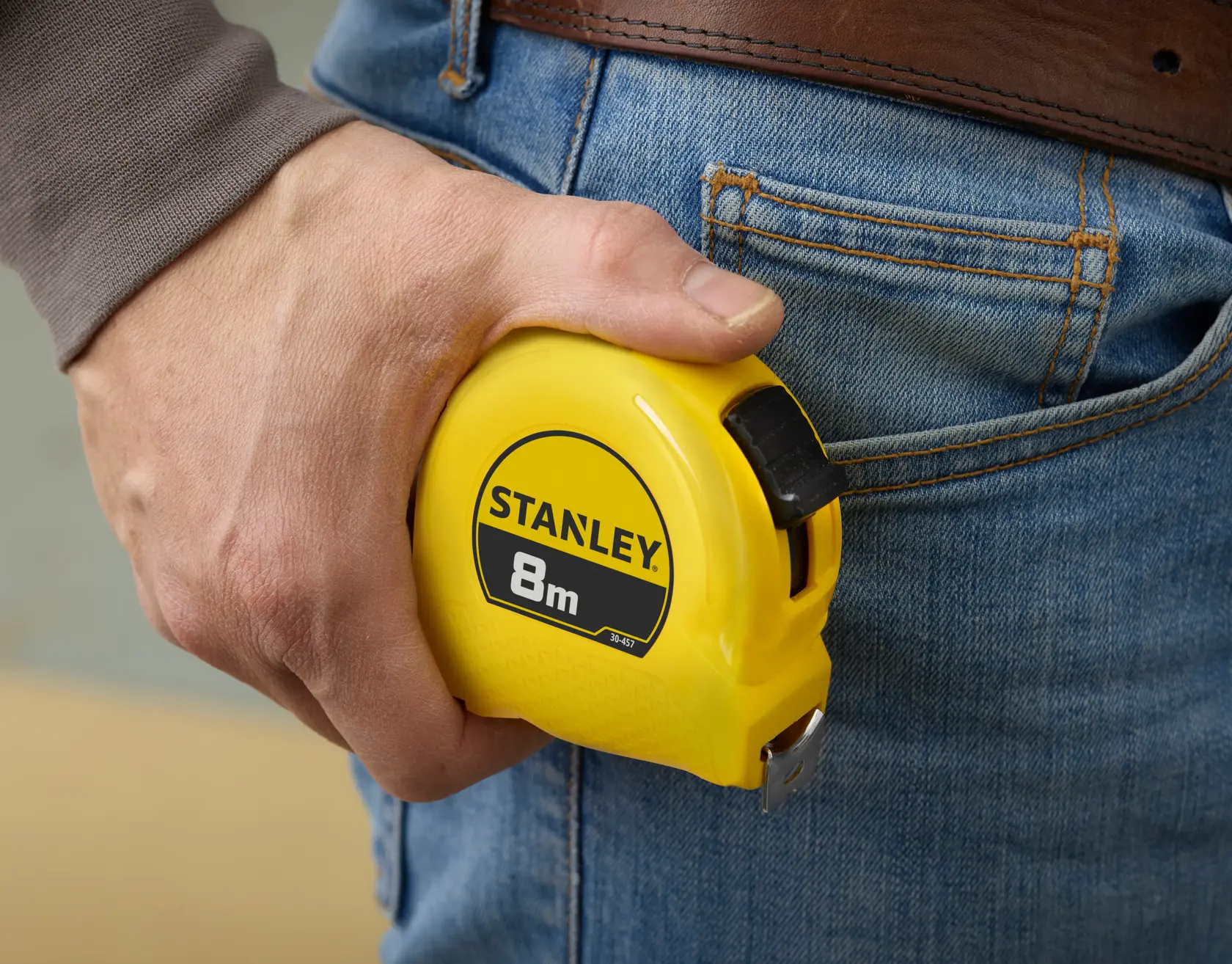 Foto vom STANLEY 0-30-457 8m Maßband in der Hand neben einer Jeans-Tasche.
