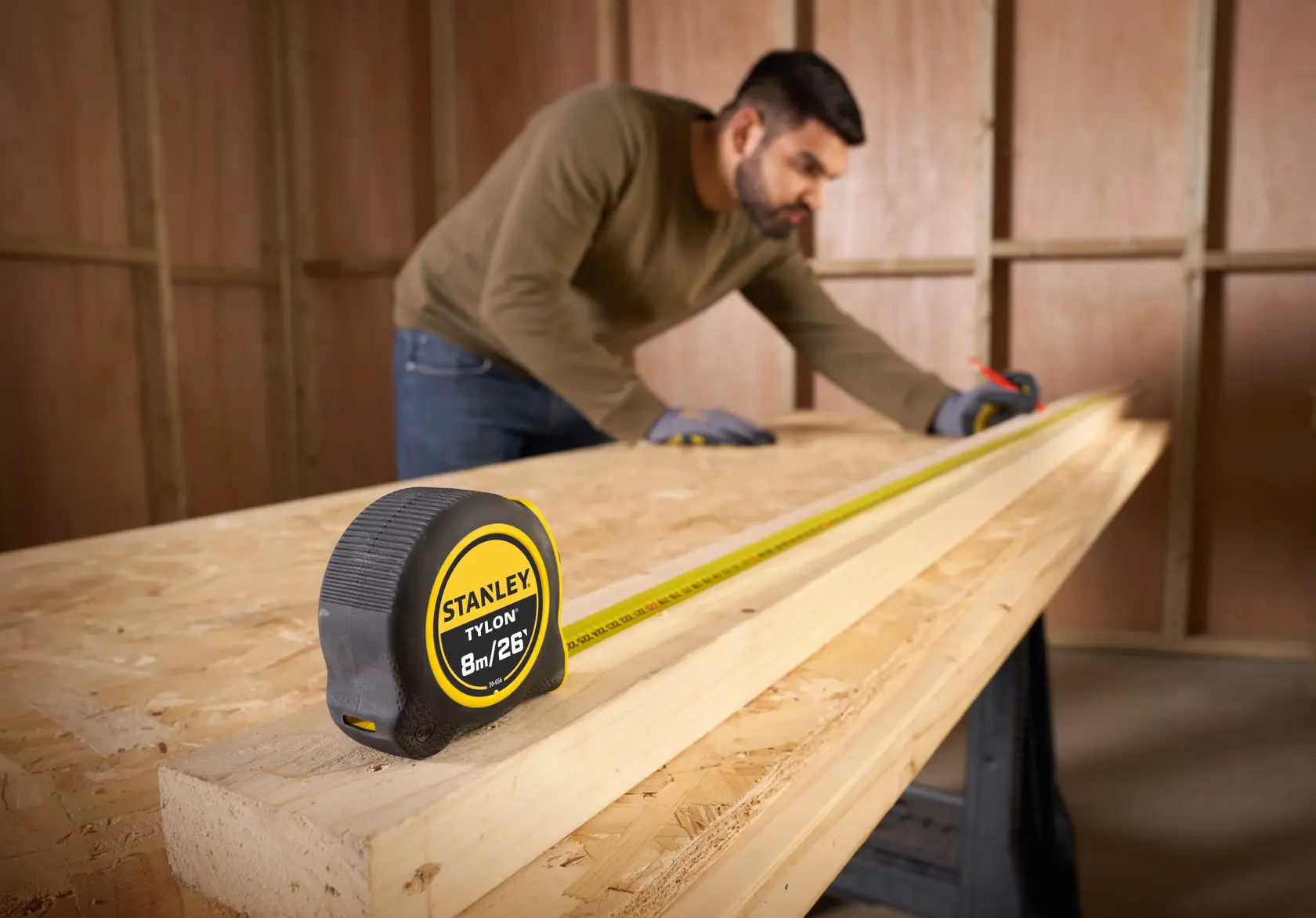 Photo of STANLEY 0-30-656 tape measure on a wooden workbench with person measuring long wooden boards.