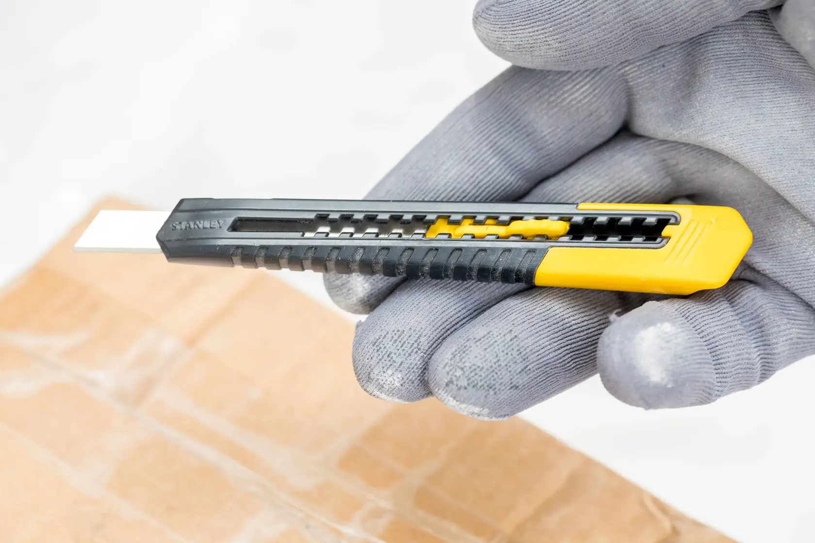 STANLEY 2-10-150 utility knife with black and yellow handle, shown held above a cardboard box.