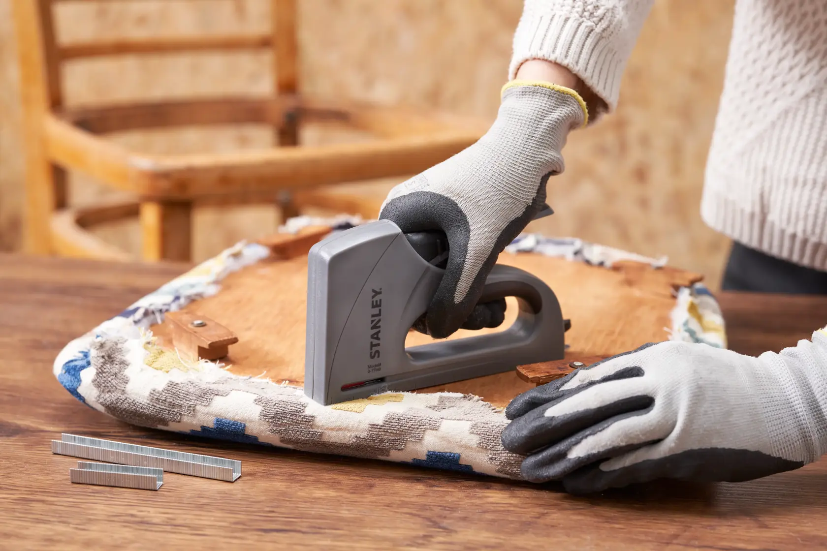 STANLEY 6-TR40 hand stapler being used for upholstery on a wooden chair seat, gloves worn.