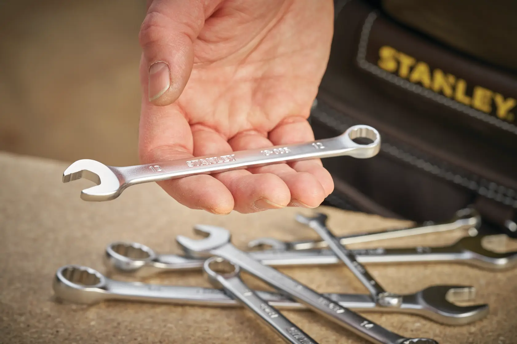 STANLEY FMMT13031-0 combination wrench held in hand, several wrenches on wooden surface, close-up.