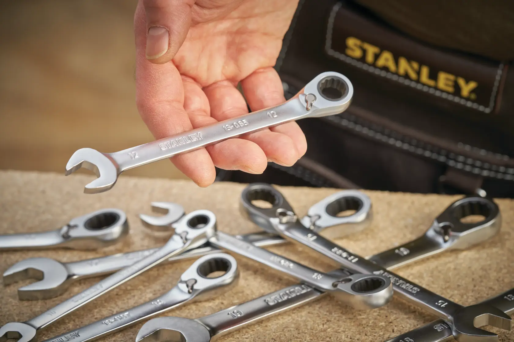 Photo of STANLEY FMMT13095-0 ratcheting combination wrench held by hand, with other wrenches on a workbench.