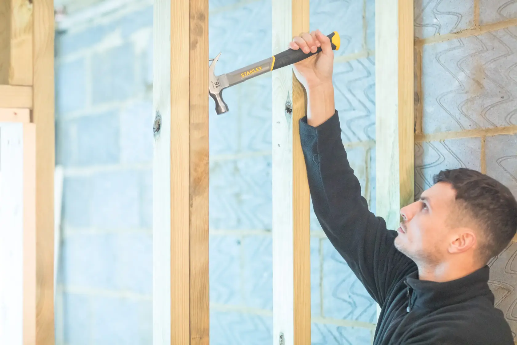 Photo of STANLEY STHT0-51309 claw hammer driving a nail into wood, held in a gloved hand.