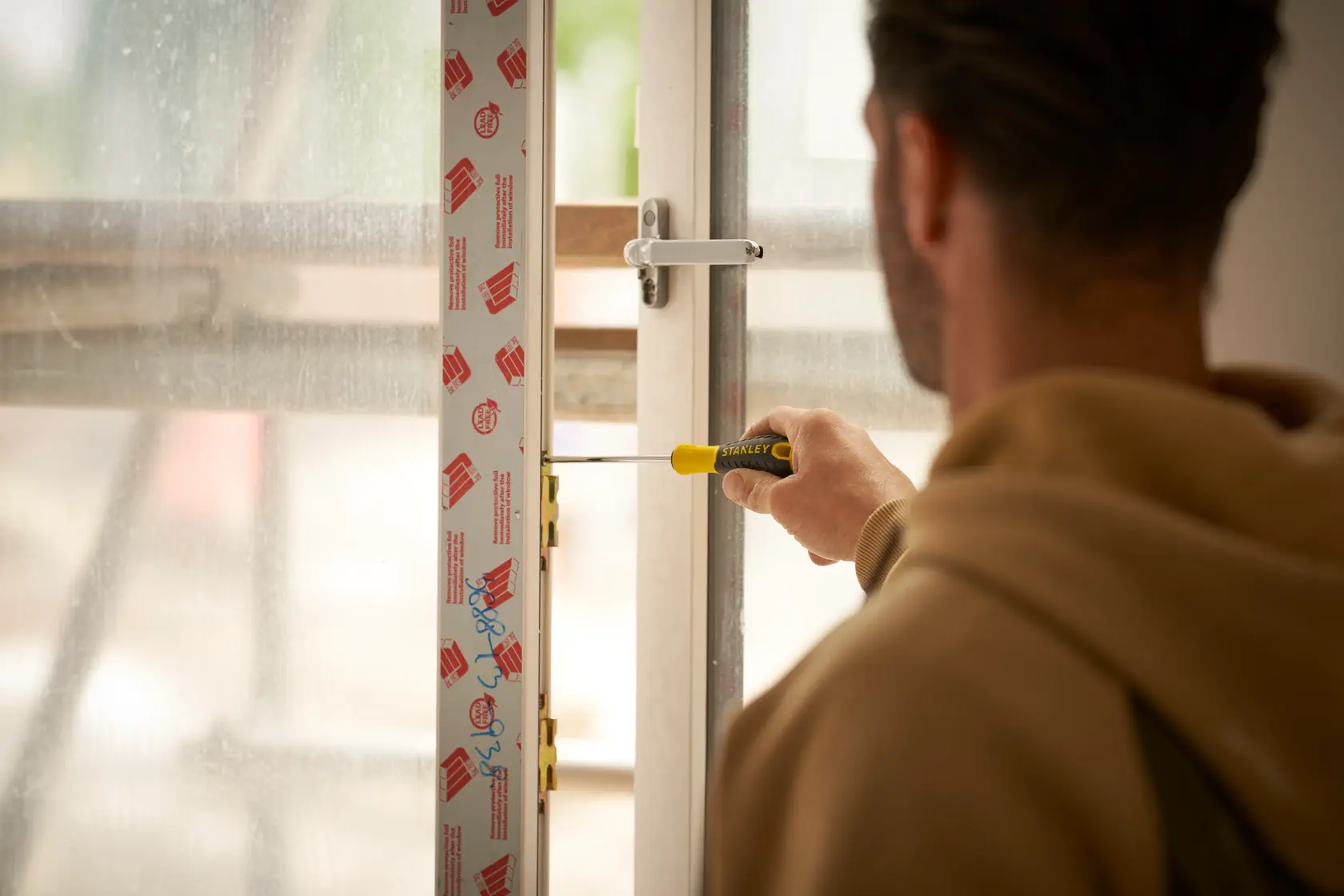 Photo of STANLEY STHT0-60335 screwdriver in use installing a window lock, held by a person in indoor setting.