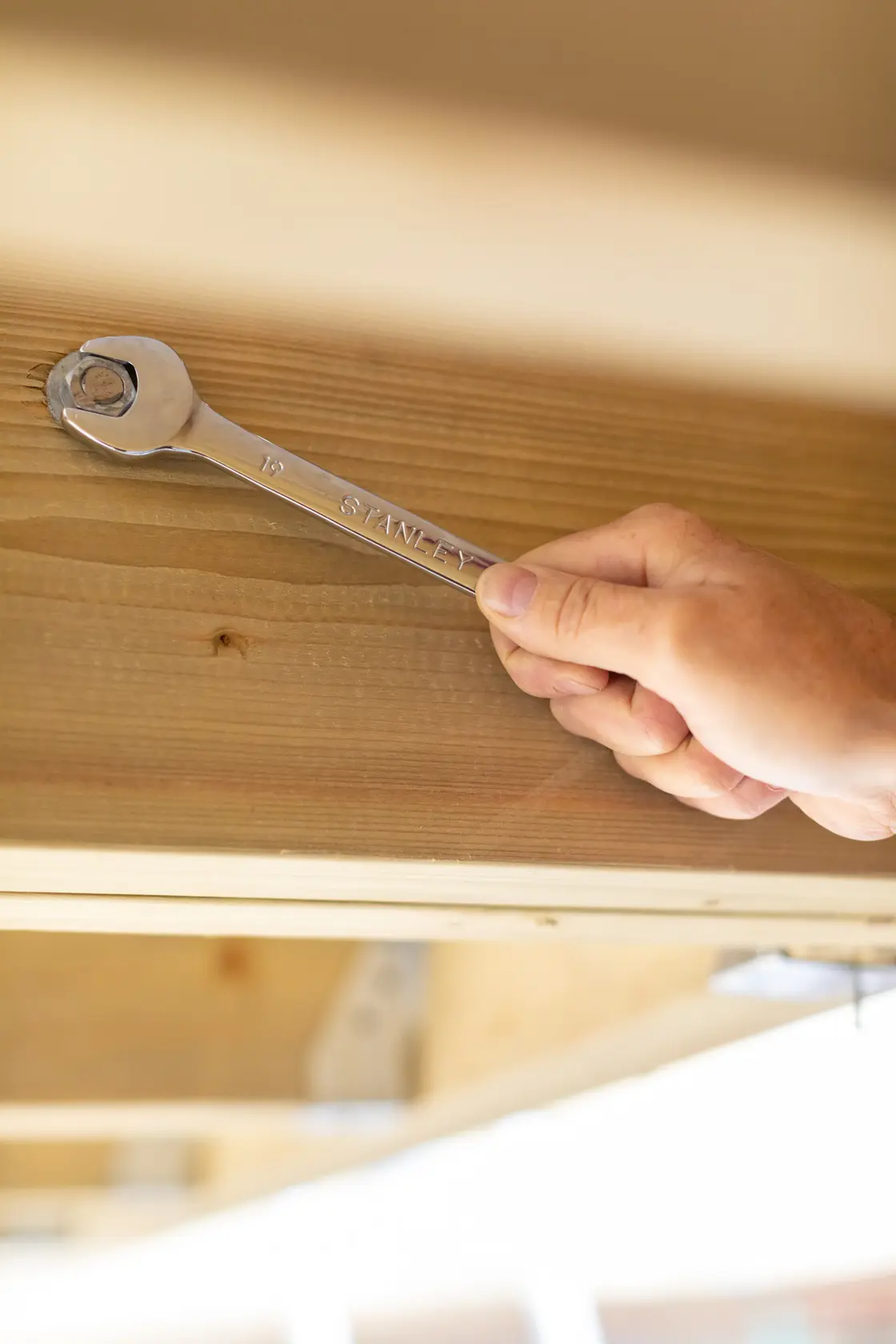 STANLEY STMT89908-0 wrench tool in hand tightening bolt on wood, photography of hardware use.