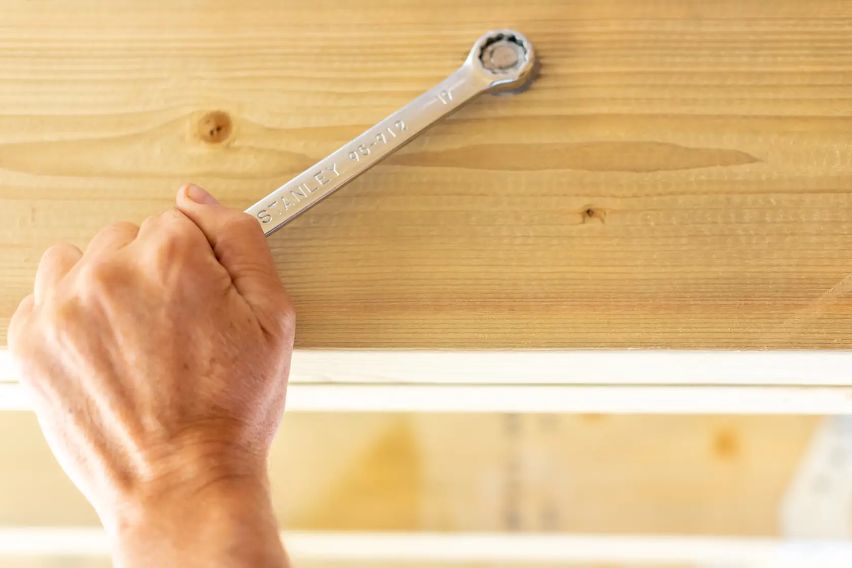Photo of a hand using STANLEY STMT95908-0 ratcheting wrench on a wood beam, close-up side angle.