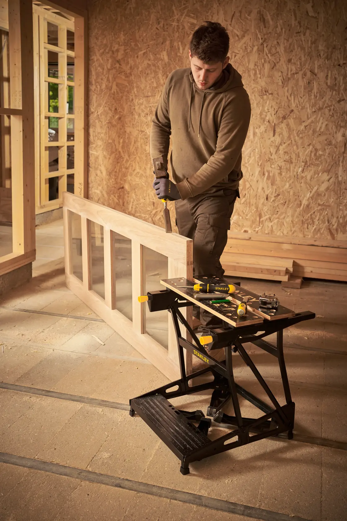 STANLEY STST83400-1 foldable workbench with tools, shown in use in a woodworking workshop.
